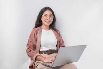 Smiling young Asian business woman sitting down and holding a laptop open over isolated white background.
