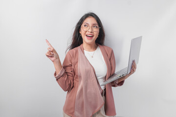 Excited young Asian business woman holding a laptop while pointing to the copy space beside her on...