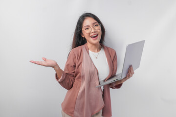 Excited young Asian business woman holding a laptop while pointing to the copy space beside her on...