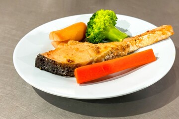 Healthy food. Grilled salmon served with steamed broccoli and carrots on white plate, epitomizing...