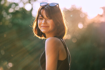 A beautiful young teenage girl dressed in a black dress cheerfully smiling at the camera with a warm sunset backlight. Beautiful people and a fashion concept image.