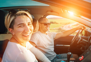 Portrait of cheerful smiling young woman with husband have auto journey inside modern car. Safety...