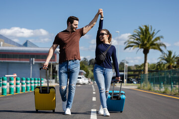 excited couple with raised hands walking to the airport to go on a trip