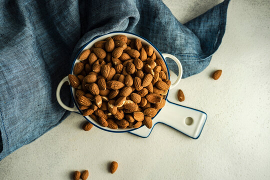 Ceramic bowl with organic almonds on white concrete background