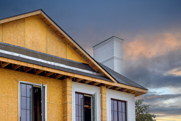 An under construction house has joist framework features plywood, gutter holders, soffit fascia trim installed