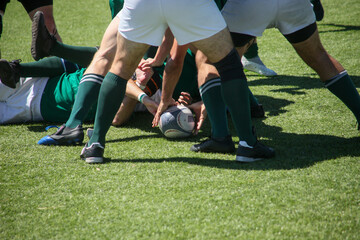 Group of men playing rugby on grass field, tackling and passing ball in action-packed match.