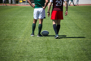 Group of men playing rugby on grass field, tackling and passing ball in action-packed match.