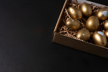 Golden eggs in paper box on dark table.