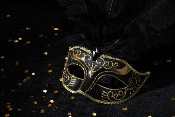 Masquerade gold mask with feathers and confetties on black background..
