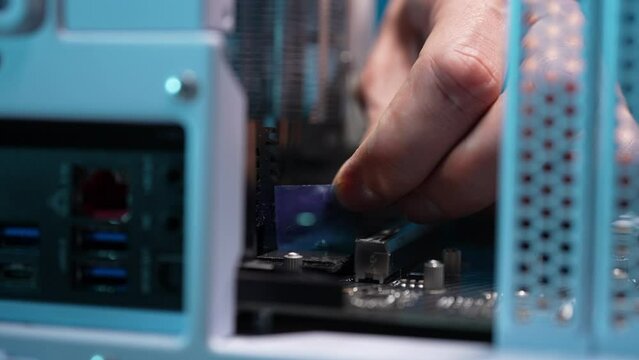 Computer repair technician male peeling tape off new SSD disk after installing in slot on motherboard. Stages of unpacking modern electronic equipment and preparing for work. Shooting in slow motion.