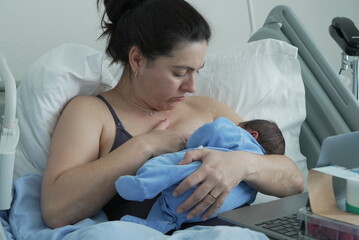 A tender moment in the hospital, a new mother breastfeeding her newborn while resting in bed,...