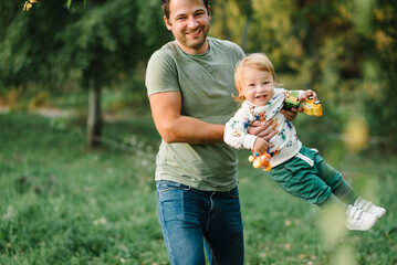 Dad and son playing at sunset. Happy son with dad standing in green grass in garden in summer. Kid...