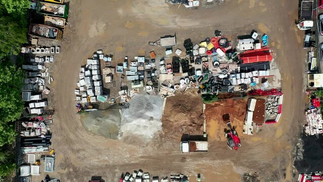 Aerial footage of an old scrap yard and builders merchants in the city of Leeds in the UK showing a digger loading a lorry surrounded by construction parts and scrap metal