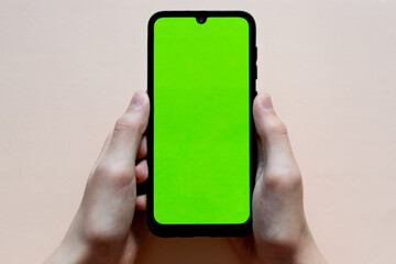 hands holding a phone with an empty green screen on a monochrome background. free space for text