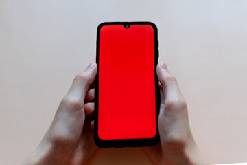 hands holding a phone with an empty red screen on a monochrome background. free space for text