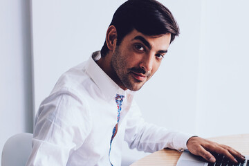 Portrait of successful indian entrepreneur sitting at desktop with modern laptop device and looking...