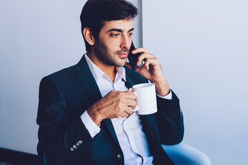 Serious indian businessman enjoying coffee break after work in company office calling to colleague...