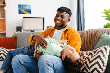 Handsome, smiling African American man, young father fooling around with his little son, tickling