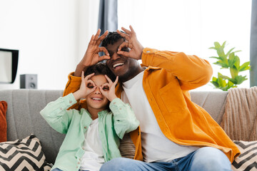 Happy African American father and little son fooling around together showing eyeglasses with fingers