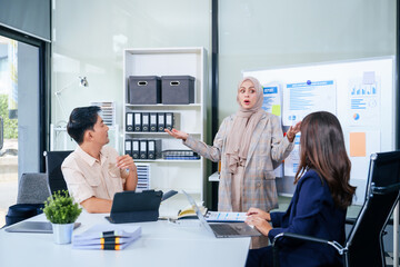 A multicultural team of professionals, including male and female businesspersons, convenes around a desk with tablets, discussing strategies illustrated on a whiteboard during a dynamic presentation.