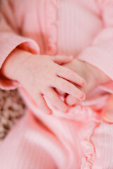 A newborn baby girl has her hands together. She is dressed in an all pink feminine outfit.