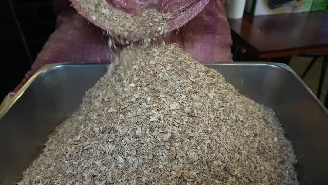 Hands mix dry sawdust in a metal tray, readying it for grilling to infuse a rich, smoky flavor into foods.