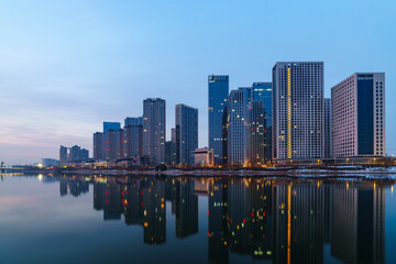 Fototapeta premium Skyscrapers reflection upon a river at dawn in Tongzhou District, Beijing, China, which is a newly-established business district