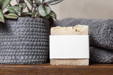 Soap bar with blank label near grey towels and green potted plant on wood, mockup