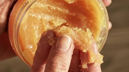 Hand trying cosmetic sugar body scrub with enzymatic exfoliating particles from jar. Body skin care concept.