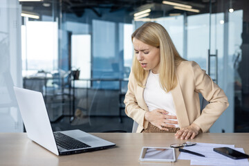 Businesswoman experiencing stomach pain while working on laptop in modern office