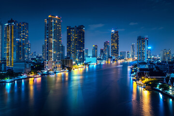 Fototapeta premium A glistening city skyline illuminated against the night sky, with dazzling lights reflecting in the calm waters of an urban river.