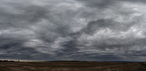 Dramatic gray storm clouds building above a dry prairie farm field.  The clouds warn of an impending storm.
