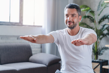 Close up portrait of middle age adult man doing squats and exercising on yoga mat in living room at...