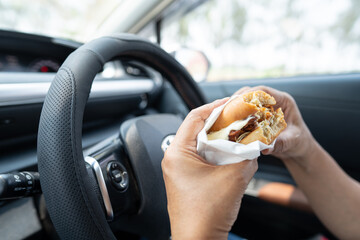 Asian lady holding hamburger and French fries to eat in car, dangerous and risk an accident.