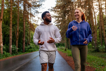 Two friends running through a scenic forest path, sharing joy and fitness. Wearing hoodies and...