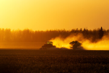 Obraz premium Tractor with a seeder is working in the dust in golden sunset light.
