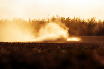 Tractor with a seeder is working in the dust in golden sunset light.