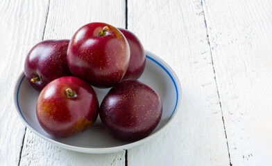 ripe plums in a white plate on a white wooden table with a copy space