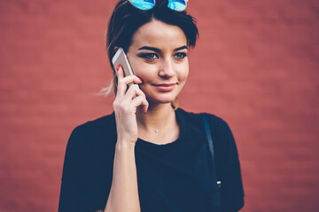 Positive carefree female teenager 20s with sunglasses looking away while holding mobile phone and...