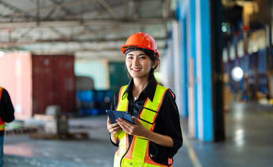 A woman wearing a safety vest and an orange helmet is holding a tablet in her hand. She is smiling and she is happy