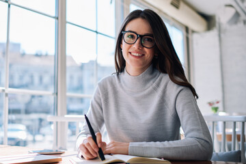 Portrait of happy young trendy woman working as journalist resting at cafeteria, successful hipster...