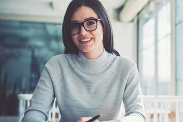 Smiling brunette hipster girl wear in fashionable spectacles studying at coworking space and...