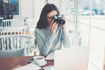 Talented creative hipster girl making pictures using old fashioned vintage camera indoors, young...