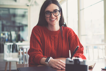 Successful female teenager spending free time at cozy cafeteria while looking at camera, positive...