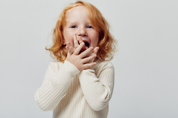 Innocent little girl with red hair expressing astonishment in front of white background