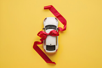 White model car with red ribbon bow on a yellow background. Car as gift, surprise. Present concept. Close up full length size of toy car isolated on color backdrop, copyspace. Rental, auto dealership