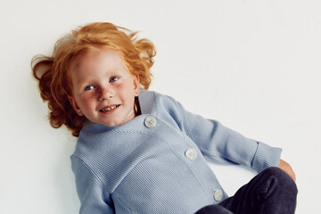 Little girl with red hair in light blue coat and jeans laying on floor in cozy fashion style beauty...