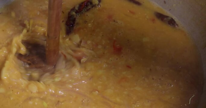 Adding boiling dal lentil into bagar tadka with deep fry tomato onion garlic cumin red dry chilli spice stair cooking dal ghotni whisk 