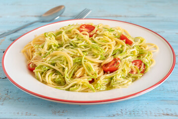 Vegetarian pasta with zucchini and cherry tomatoes on ceramic plate.