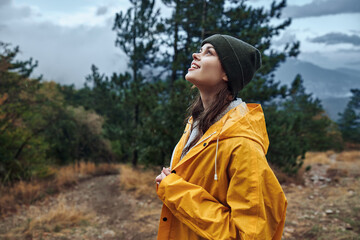 Woman in a yellow raincoat standing on a hill, contemplating the sky and embracing the beauty of...